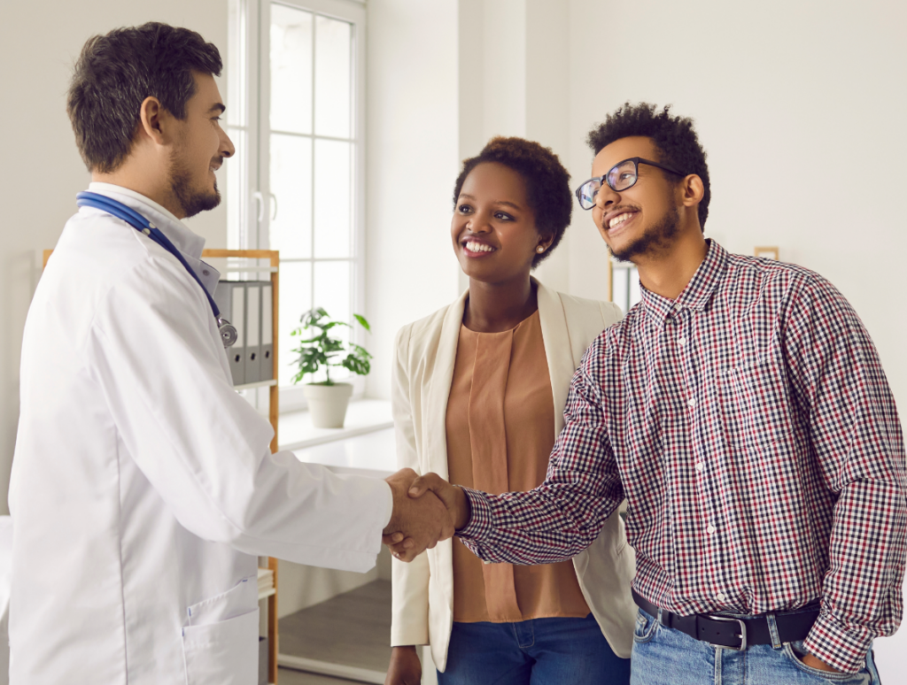 A doctor in a white coat shakes hands with a smiling man in glasses and a checked shirt, while a woman in a beige blazer stands beside them, celebrating successful hyperbaric oxygen therapy in a bright office setting.