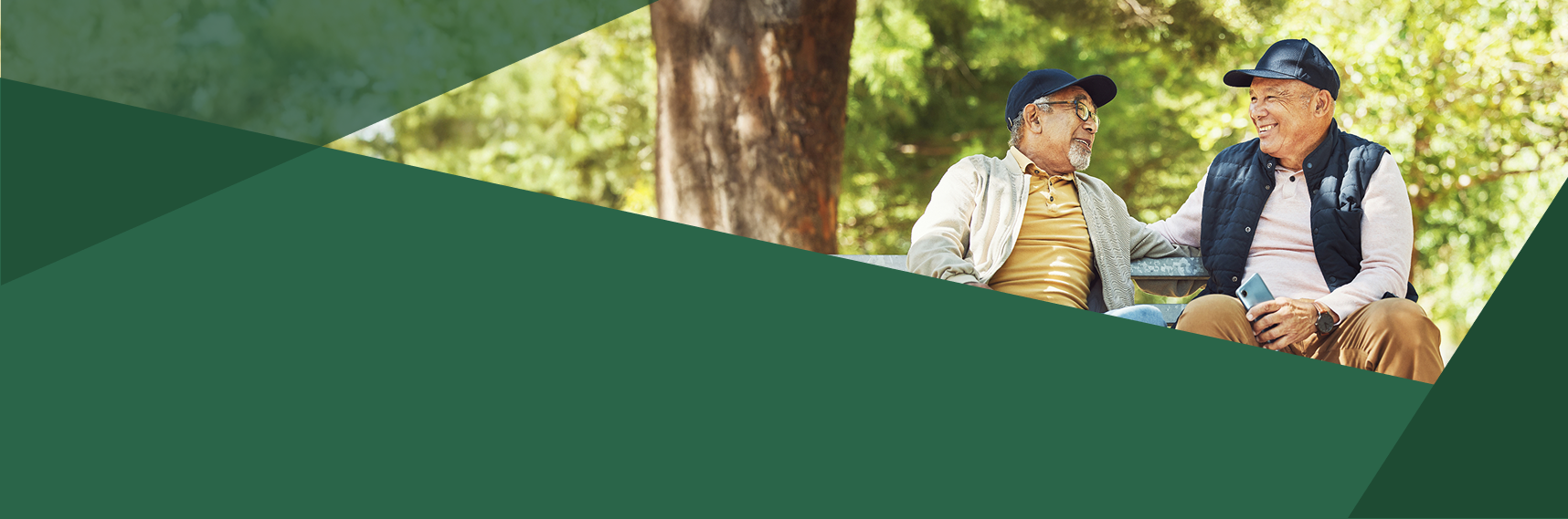 Two older men sit together on a park bench, smiling and talking, surrounded by trees. The lower half of the image is covered by overlapping green geometric shapes.