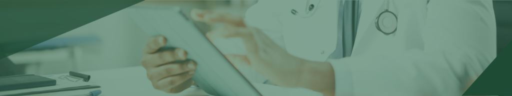 A doctor in a white coat uses a tablet at a desk, with a stethoscope visible around their neck and paperwork nearby.